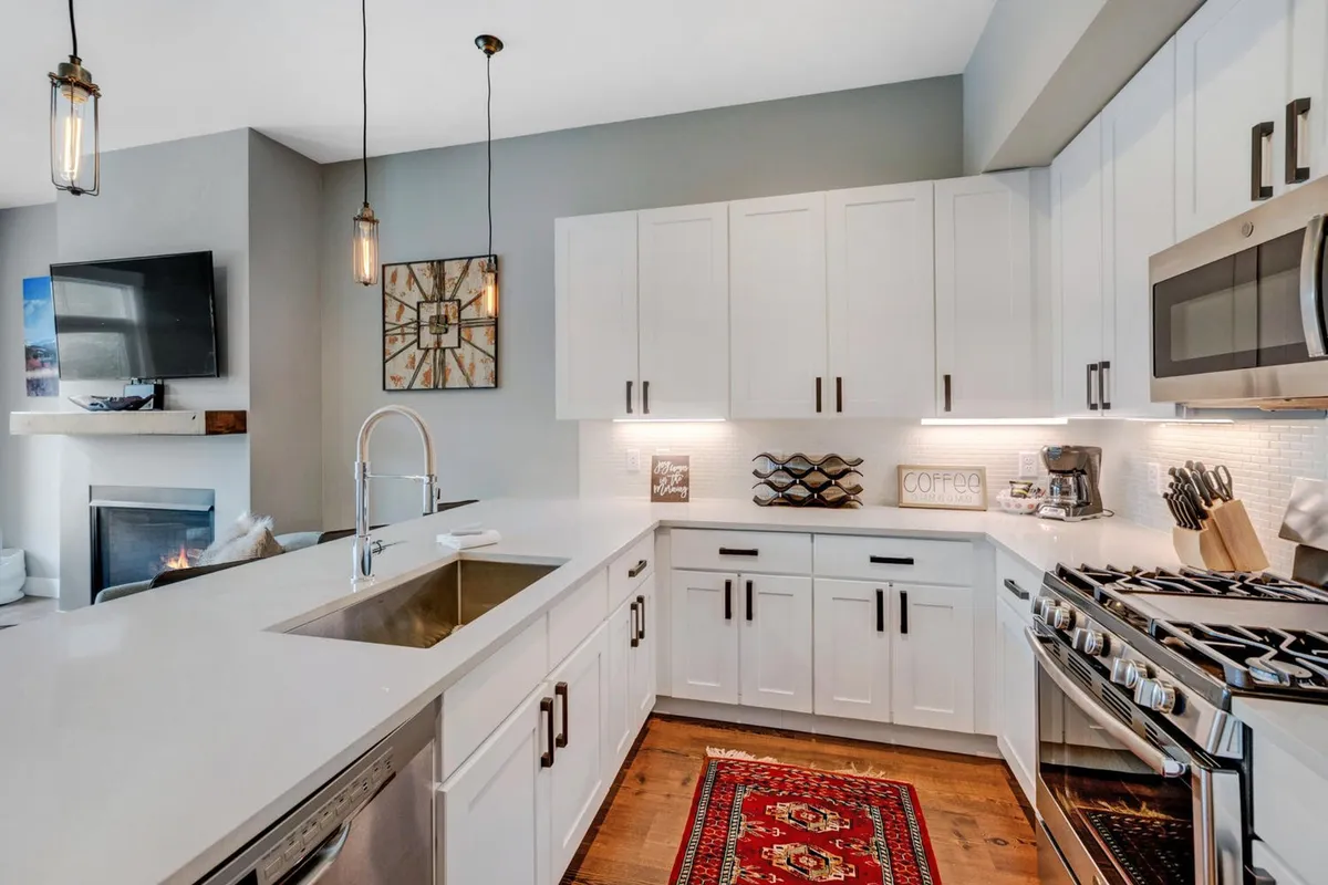 A bright, modern kitchen featuring stainless steel appliances, white cabinetry, a central kitchen island, and a cozy rug. The space is designed for both cooking and gathering, with ample counter space making it easy to prepare meals.