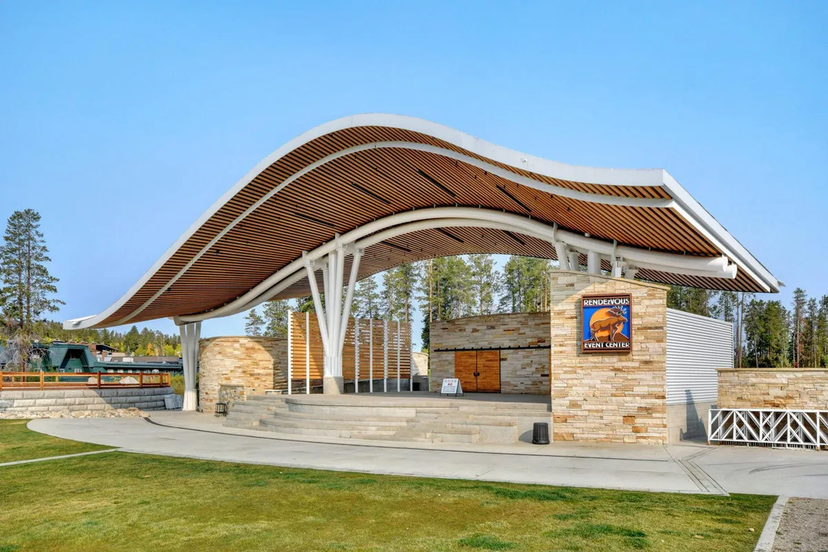 This image displays the Hideaway Park amphitheater with its distinctive curved roof structure and stone facade, set in an open stage area. The scene is inviting, with ample space for concerts, community events, and family-friendly outdoor gatherings.