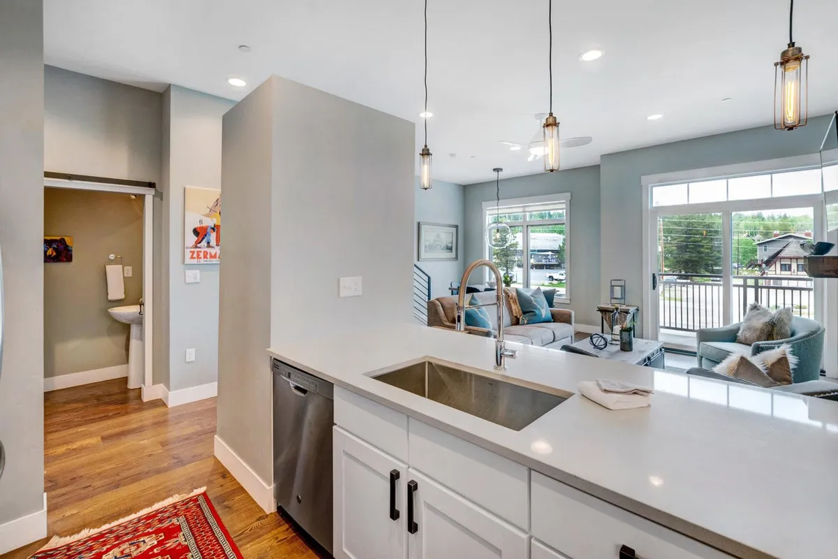 A bright, open-concept space combining a kitchen island, a view into the living area, large windows letting in natural light, and a decorative rug. The scene is lively yet cozy, evoking togetherness and the aroma of fresh coffee in the morning.