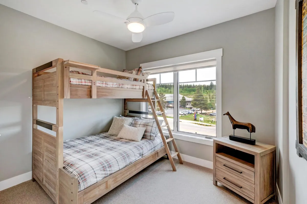 A playful bunk bedroom featuring a sturdy bunk bed with comfortable bedding and a window offering a view outside. The room is cheerful and designed for both sleep and play, making it appealing to families and groups.