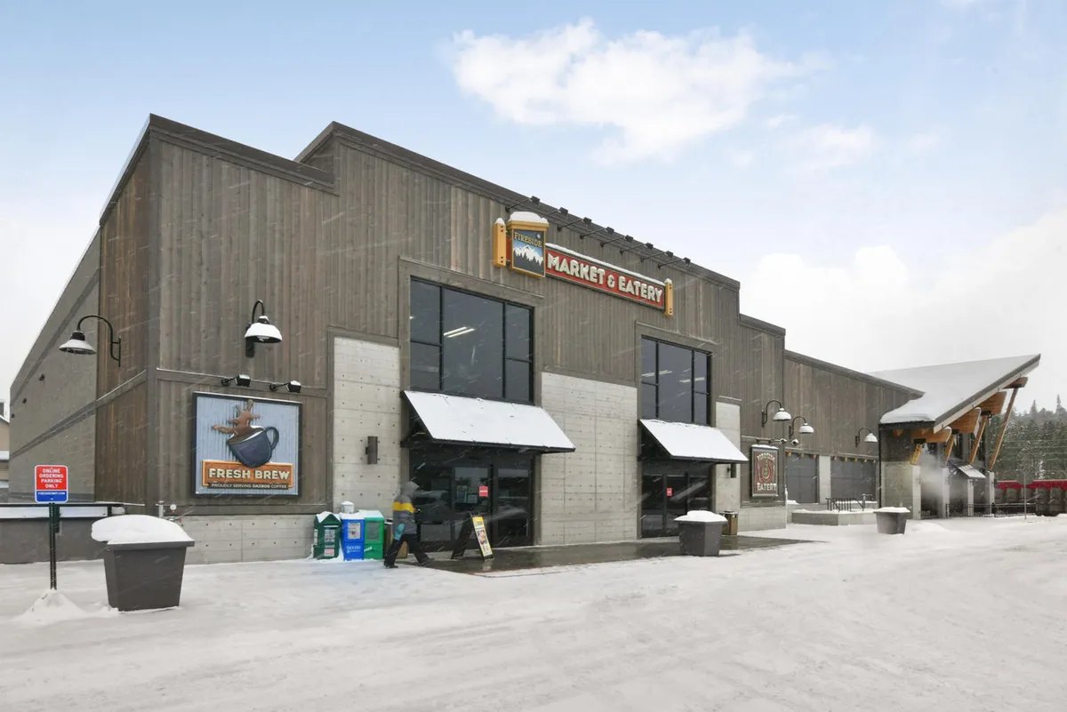A welcoming exterior shot of a market with a prominent sign, entrance doors, and a snow-covered ground. The scene captures people engaging in shopping and socializing in a cozy, wintry setting.
