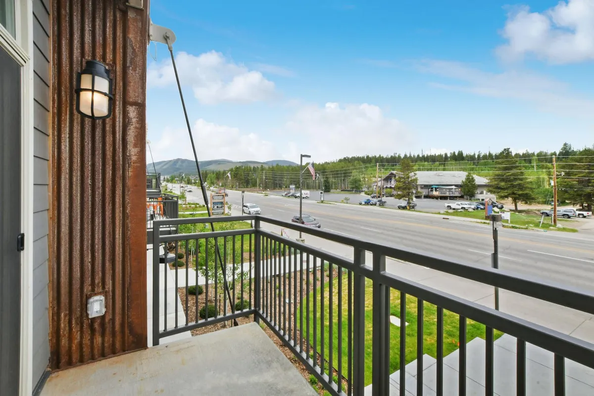 A balcony scene with a sturdy railing overlooking the town’s streets, neighboring buildings, and mountain backdrop. The vantage point invites viewers to imagine people-watching, celebrating local events, or starting a downtown adventure just outside the building.