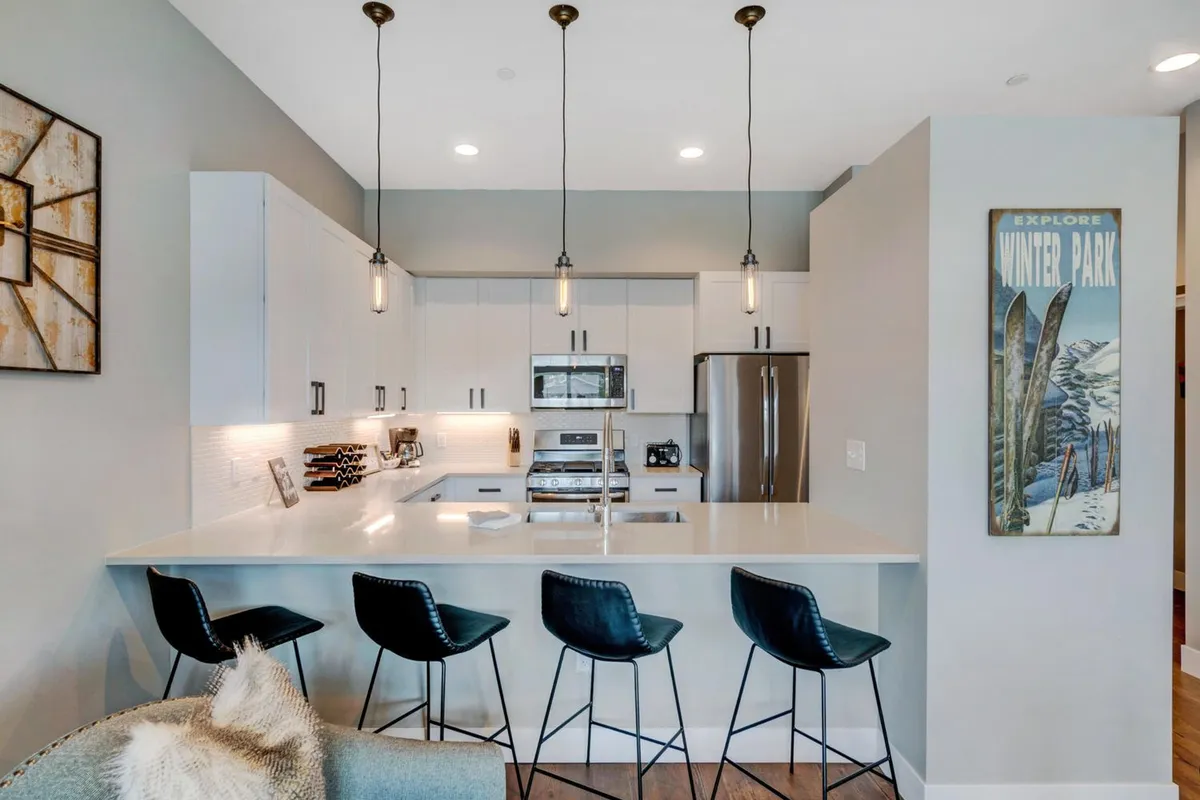 A contemporary kitchen with a large island, bar stools for casual dining, visible appliances, and stylish wall art. The setup is ideal for hosting, socializing, or enjoying a family breakfast.