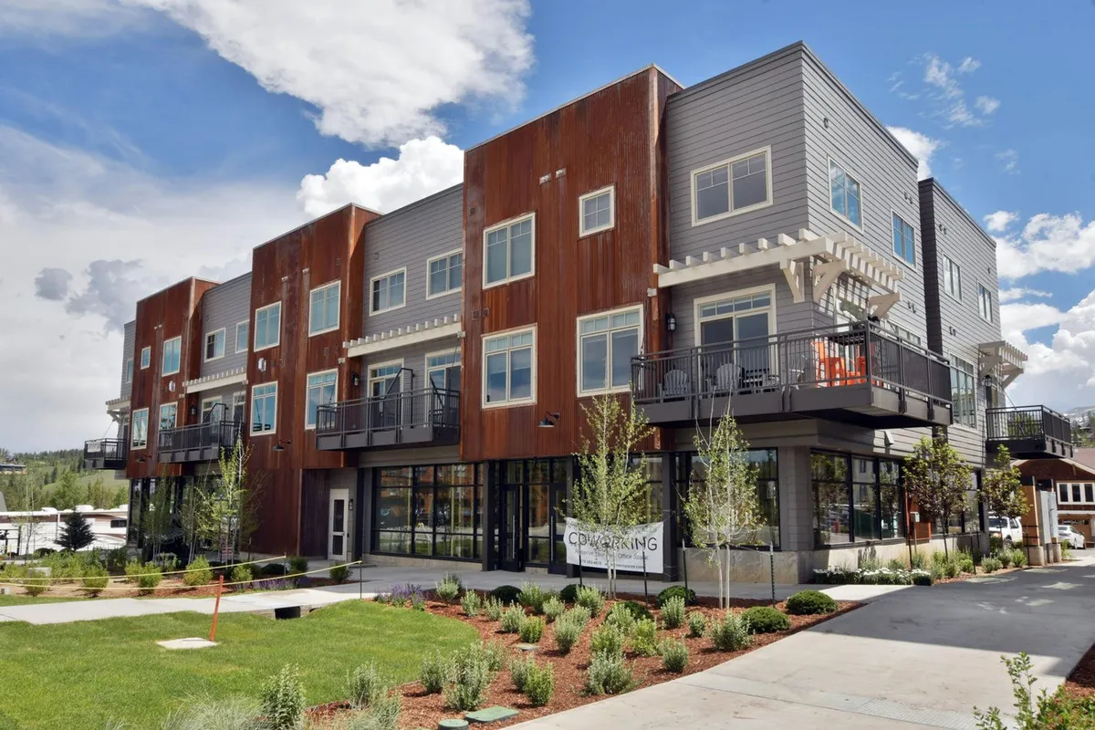 This image showcases the modern exterior of the building, featuring balconies with comfortable seating and lush landscaping. The scene is alive with people enjoying the outdoor spaces, hinting at opportunities for morning coffee or sunset toasts while taking in the mountain air.